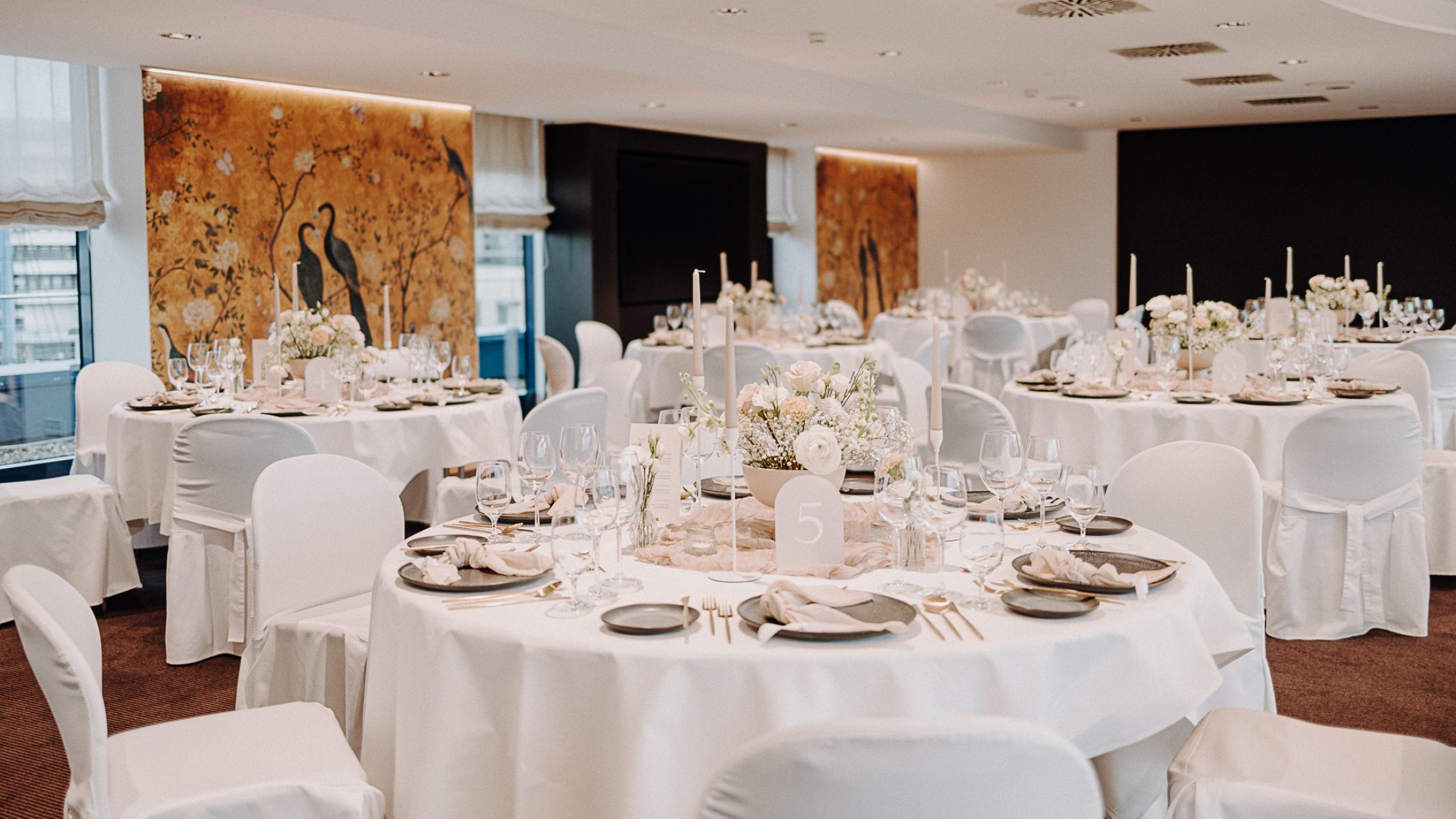 Hochzeitstische eingedeckt mit goldenem Besteck und Tisch Deko und Goldener Wand im Hintergrund