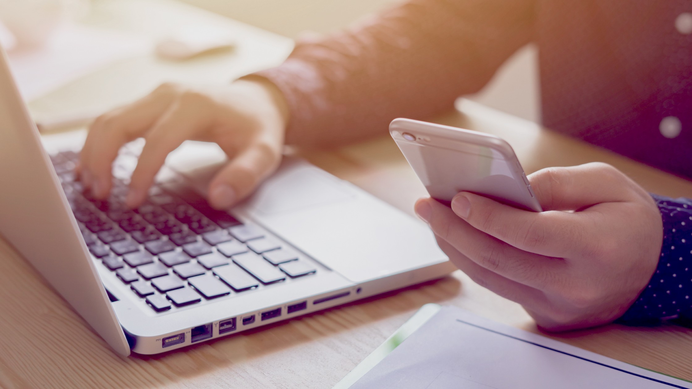 Person sitzt am Laptop und hat Ihr Handy in der Hand