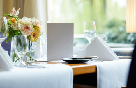 Nahaufnahme eines Tisches im Parkrestaurant mit grauer Menükart und frischen Blumen