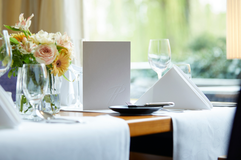 Nahaufnahme eines Tisches im Parkrestaurant mit grauer Menükart und frischen Blumen