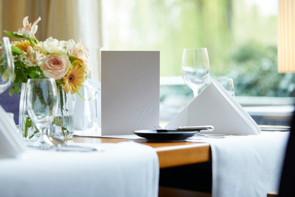 Nahaufnahme eines Tisches im Parkrestaurant mit grauer Menükart und frischen Blumen