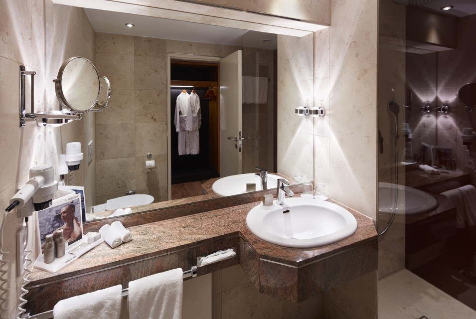 Blick ins Badezimmer in den Spiegel. Man sieht La Biosthetique Produkte auf der Ablage stehen und kann durch die Glastrennwand in die Dusche blicken