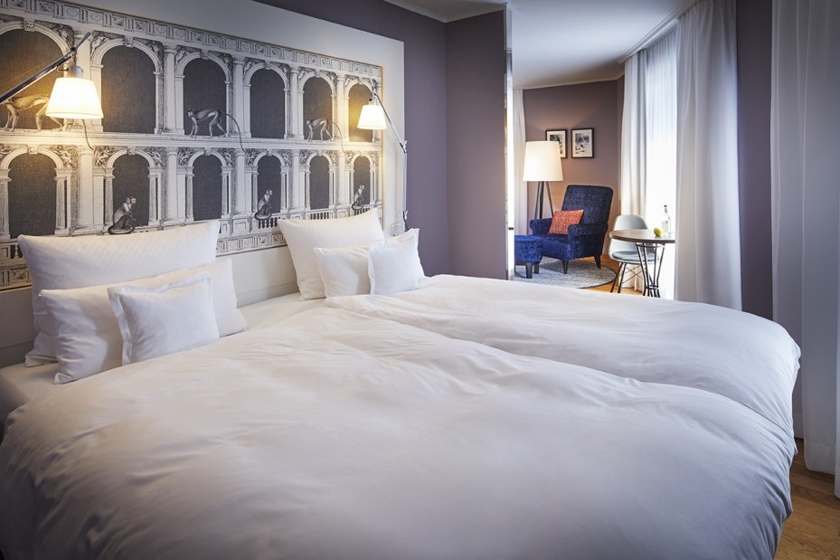 Doppelbett mit schöner Tapette am Kopfende und Blick in den hellen Wohnbereich