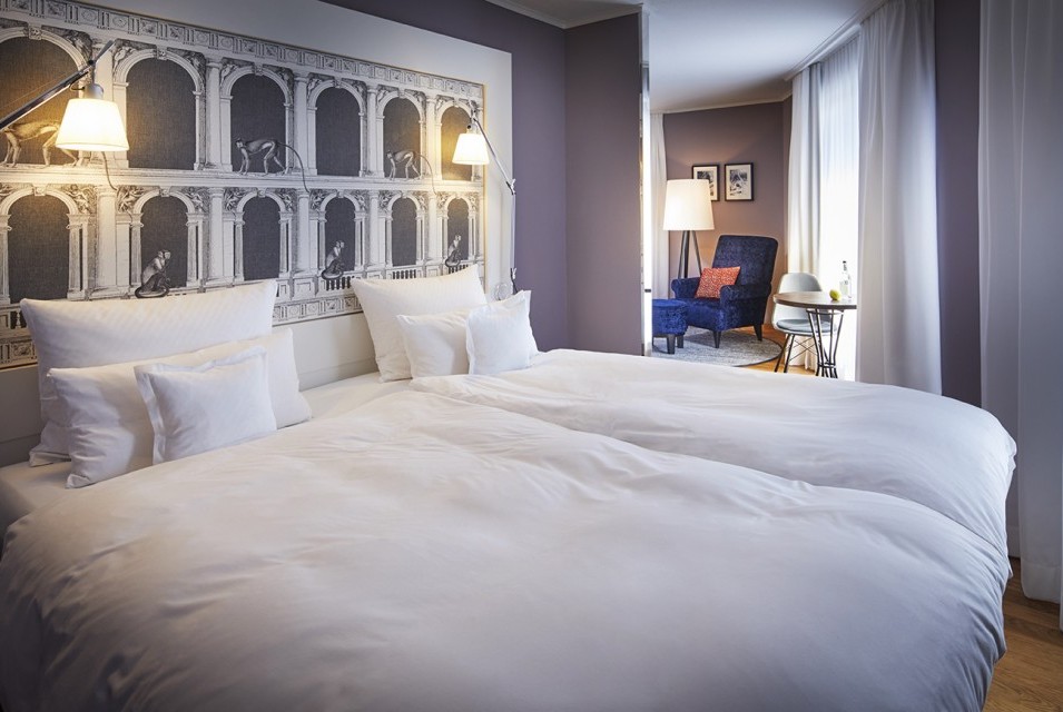 Doppelbett mit schöner Tapette am Kopfende und Blick in den hellen Wohnbereich